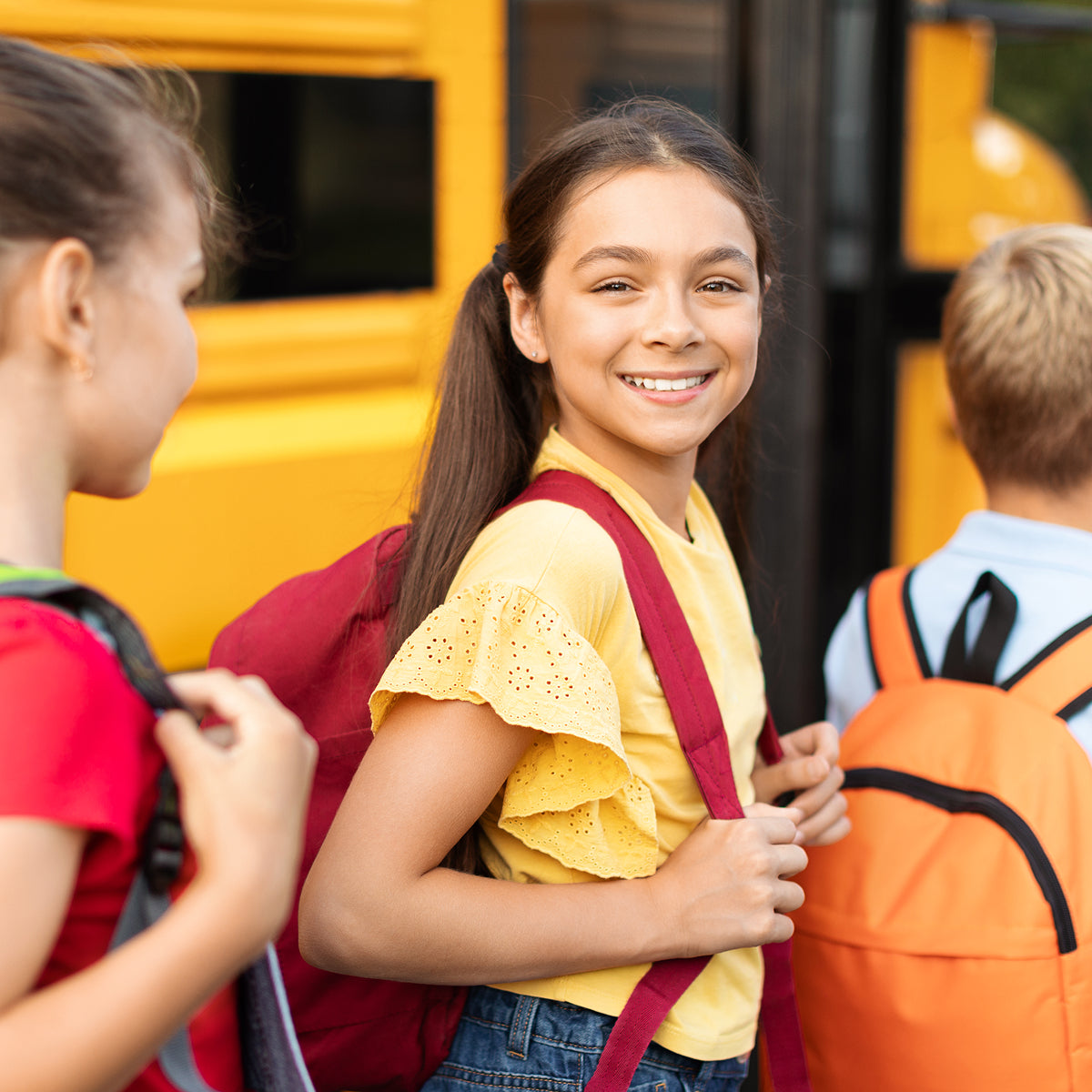 Children with backpacks in front of a yellow school bus