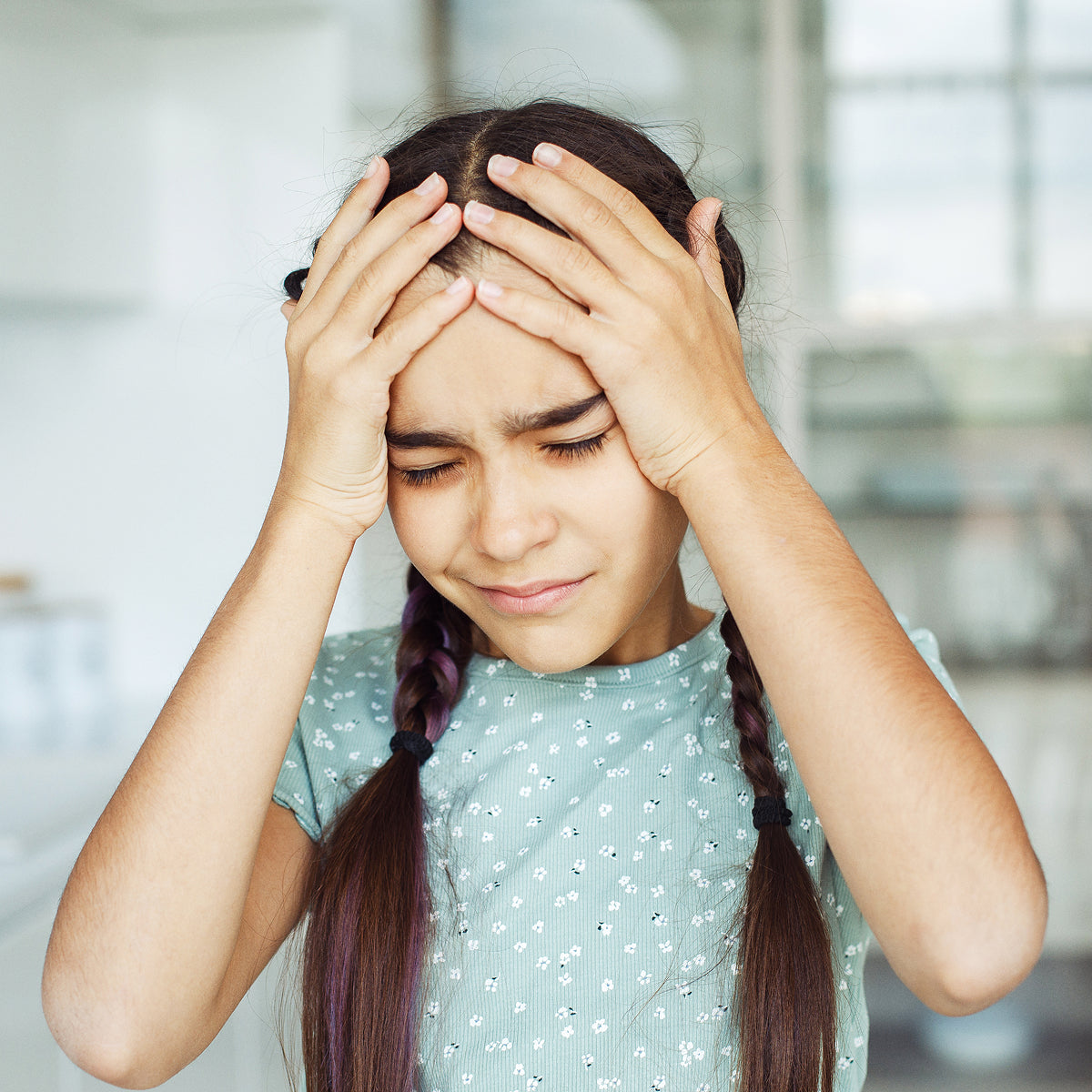 A young girl holding her head in her hands.