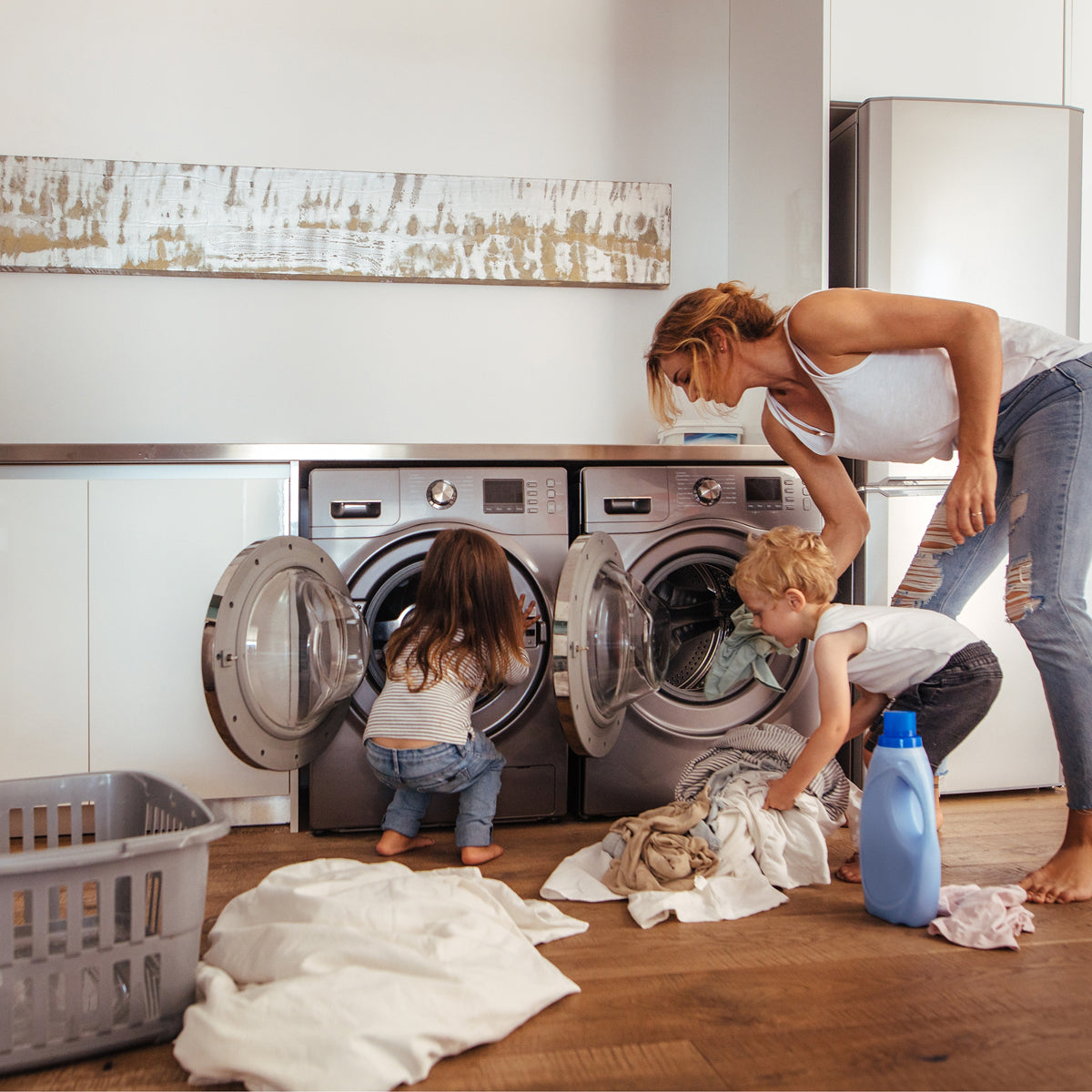 A woman, a young girl, and a young boy doing laundry together. They are all wearing jeans and white shirts. 