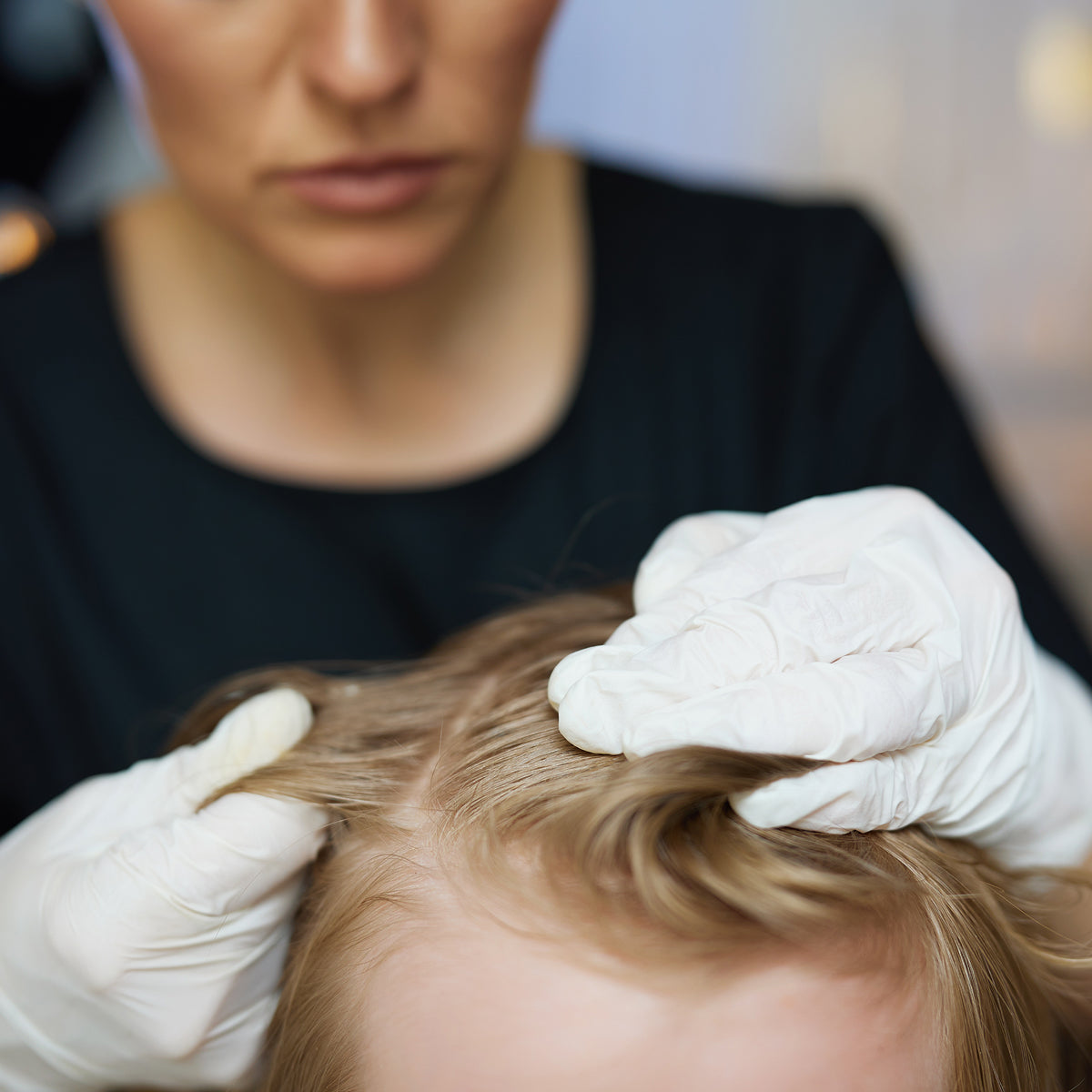 Person with white gloves examining child's hair