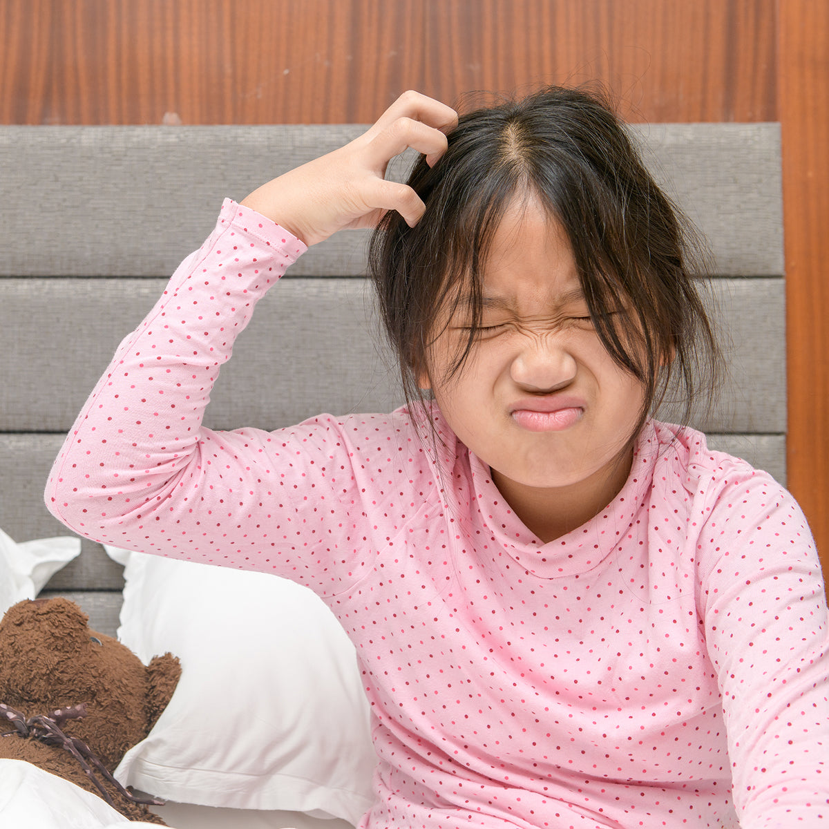 Child in pink pajama with a teddy bear on a bed