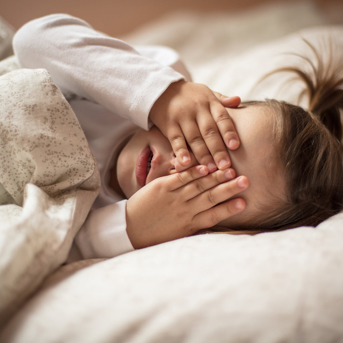 Child lying on a bed with hands covering eyes