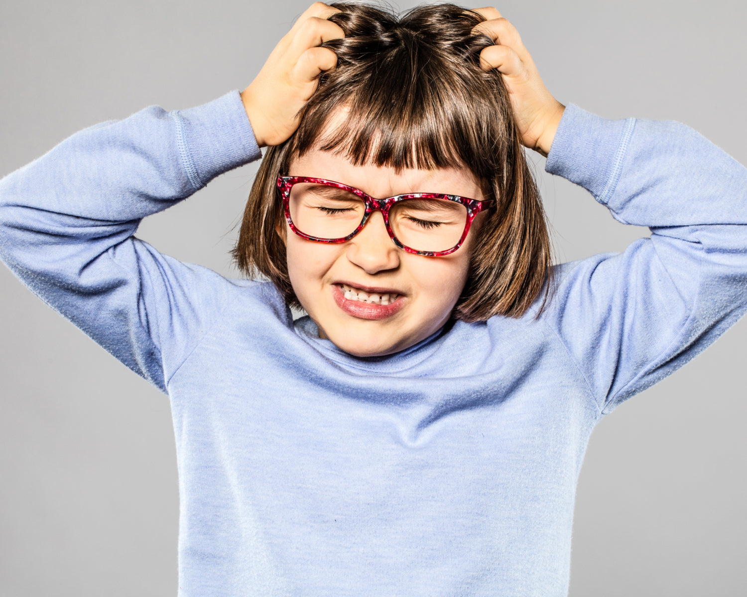 Child with glasses scratching head against a gray background
